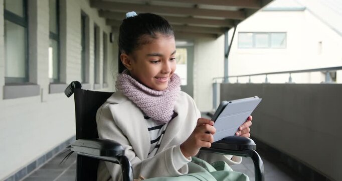 African schoolgirl in wheelchair using tablet, tapping after alert, wearing scarf, backpack on lap