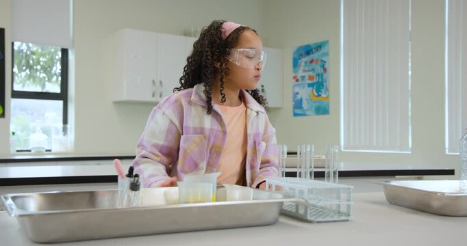 Teenage female student inspecting tray, drawing liquids with pipette into test tubes for experiment
