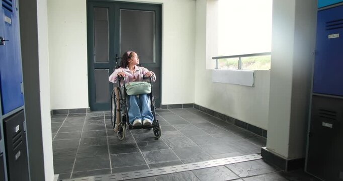 Youth woman sitting in wheelchair in lobby hands on rims watching motion outside window pale bag