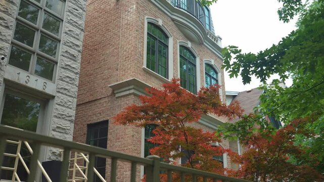 A modern luxury residential building with brick and stone facade and large grid windows surrounded by green trees. The scene shows elegant urban architecture with clean design and natural greenery in