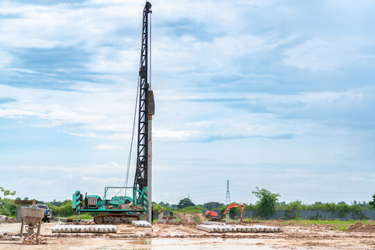 Piling machine and mini excavator working on foundation ground preparation for a new building project on a clear day.