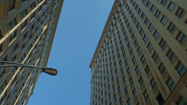 Upward perspective of tall Chicago skyscrapers creating a narrow urban canyon against a clear blue sky. Architectural lines and high-rise structures emphasize dense city development.