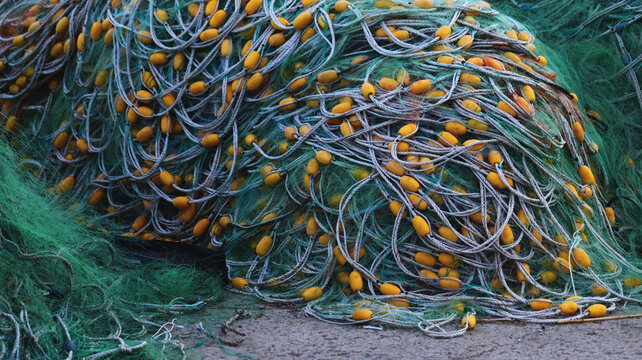 Piled Green Commercial Fishing Net with Yellow Floats and Ropes on Concrete at a Harbor