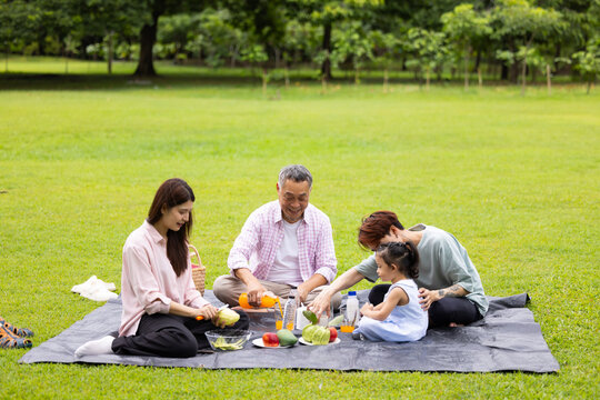 Happy Asian family having fun time on picnic at city nature park sunny day, outdoor activitie with daughter father, mother and grandfather