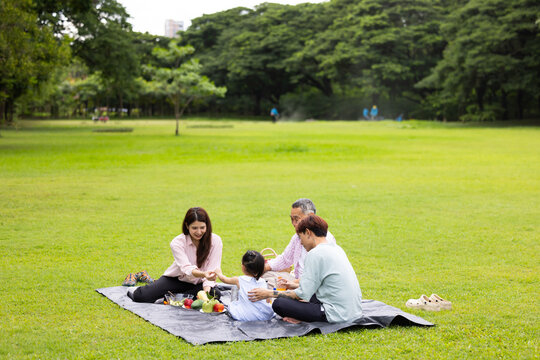 Happy Asian family having fun time on picnic at city nature park sunny day, outdoor activitie with daughter father, mother and grandfather