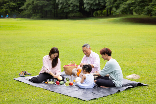 Happy Asian family having fun time on picnic at city nature park sunny day, outdoor activitie with daughter father, mother and grandfather