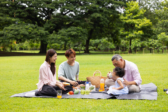 Happy Asian family having fun time on picnic at city nature park sunny day, outdoor activitie with daughter father, mother and grandfather