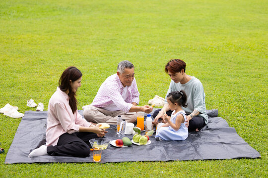 Happy Asian family having fun time on picnic at city nature park sunny day, outdoor activitie with daughter father, mother and grandfather