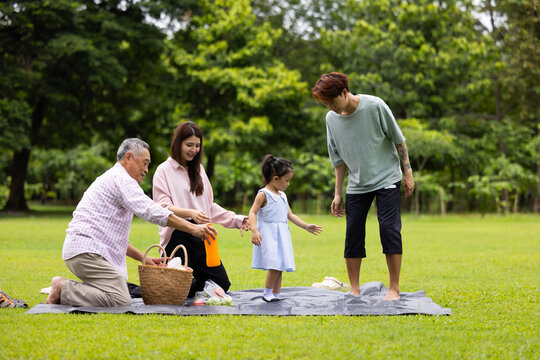 unfold picnic mat in green city park. Happy Asian family having fun time on picnic