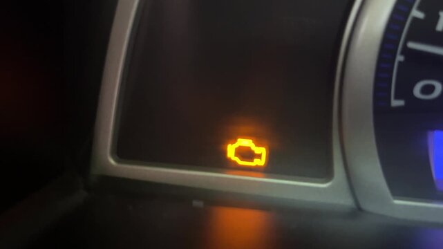Illuminated check engine light on a car dashboard close up / engine oil warning light flashing 