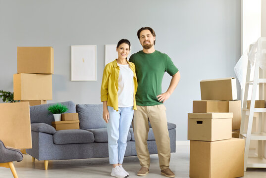 Couple moving with boxes in new home. Smiling man and woman by a sofa amid cardboard boxes in an apartment, planning layout and starting unpacking after relocation. A clear concept of moving.