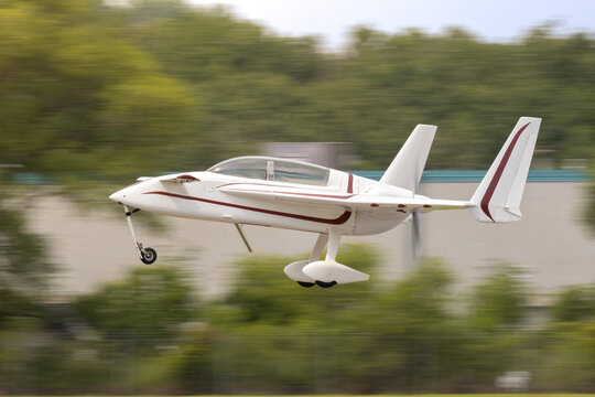 Experimental aircraft takeoff. An unconventional light airplane rushes by as it gets airborne. Equipped with canards, tail pusher propeller, retractable nose gear, bubble canopy
