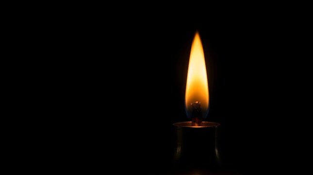 Single candle flame burning in darkness for memorial or spiritual peace