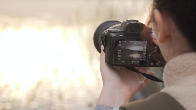 Person holds camera, focusing on bright outdoor scene. Back view shows intent to capture natural light. Soft focus background suggests serene environment. Ideal for travel, photography