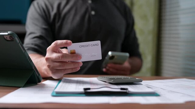 Man holding credit card enters payment details inside mobile phone near clipboard, calculator, tablet, managing debt, budget, calculating tax, cost, fee, paying bills online, checking bank accounts.
