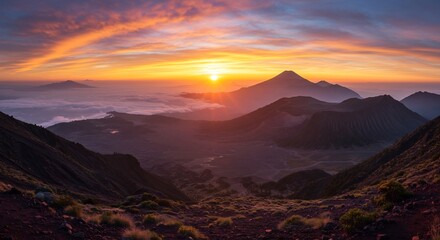 Obraz premium Volcanic Dawn Serenity: Majestic volcanic peaks rise from a misty valley as the sun ignites the sky with fiery hues of orange and gold, creating a breathtaking panorama of natural beauty at dawn.