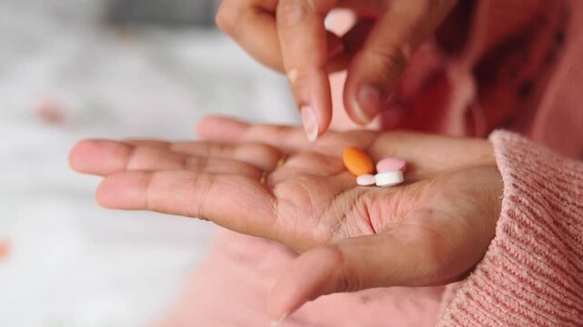 Hand holding four different pills in a home setting
