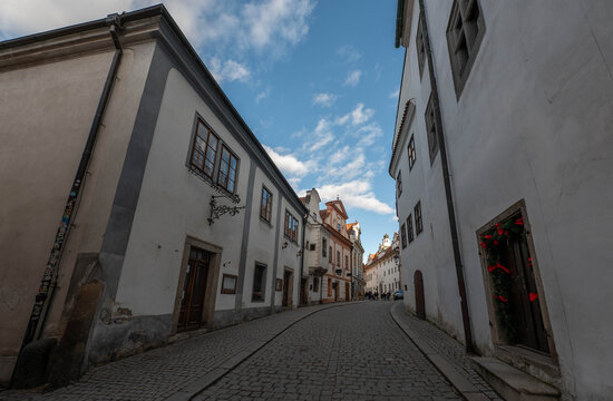 picturesque narrow historic street with traditional white buildings and cobblestone pavement under a bright blue sky with fluffy clouds in a charming European old town