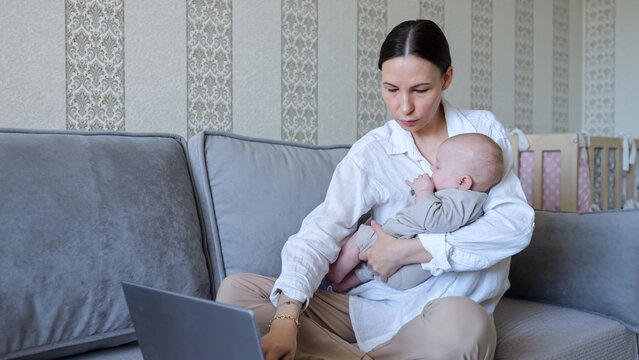 Young mother working on laptop while holding her sleeping baby and sitting on a sofa, living a freelance lifestyle balancing professional and personal responsibilities