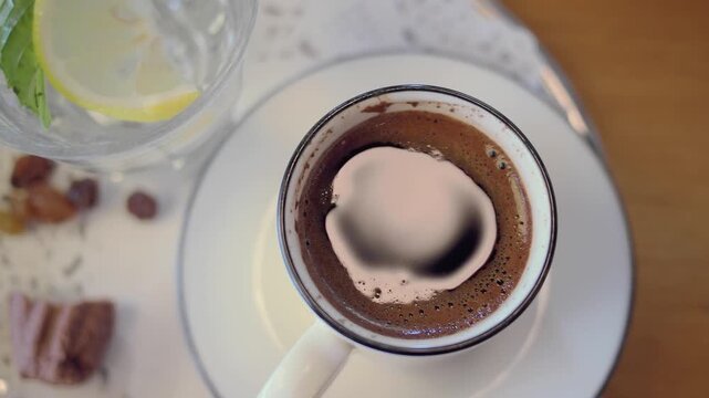 A cup of turkish coffee sits on a table in a cafe with some snacks nearby