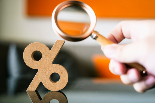 Hand holding magnifying glass over wooden percentage sign. Concept of financial analysis, interest rate research, tax inspection, and business investment strategy for commercial use.