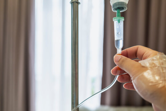 Patient hand holding and adjusting intravenous fluid drip tube in hospital room. Concept of healthcare, medical treatment, illness recovery, and clinical therapy for health industry.