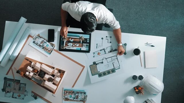 Top view of business man using tablet plan house design while sitting at meeting table with blueprint and equipment scatter around. Aerial view of civil engineer working at blueprint. Alimentation.