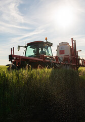 Obraz premium Farmer in tractor spraying crops at sunset