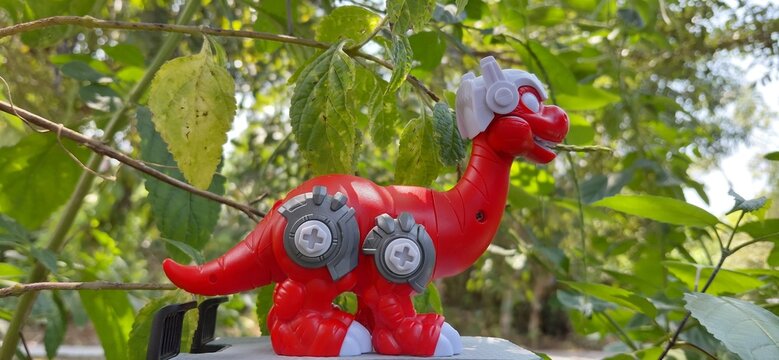 Red robot dinosaur toy figure posing among green leaves outdoor