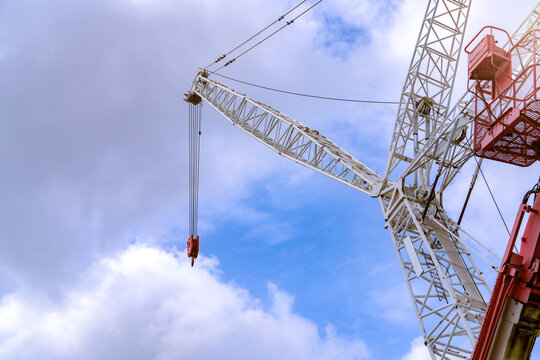 Crawler crane against blue sky and white clouds. Real estate industry. Red-white crane use reel lift up equipment in construction site. Crane for rent. Crane dealership for construction business.