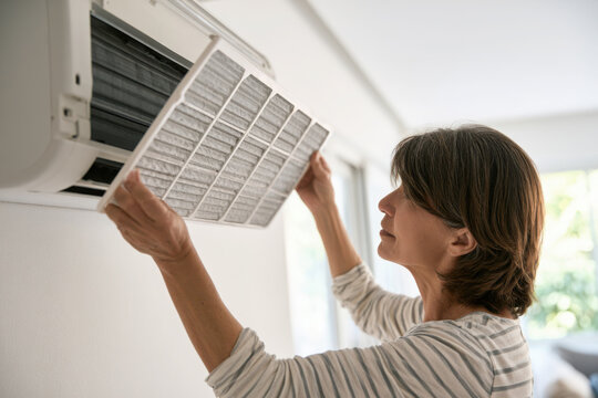 Homeowner installing a clean air conditioner filter during routine household maintenance for healthier indoor air and improved cooling performance.