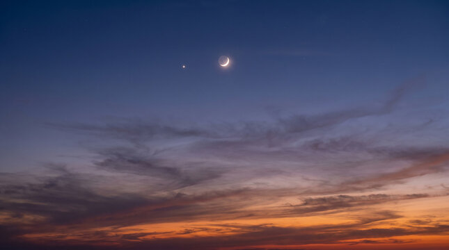 Crescent Moon And Bright Planet Visible In Colorful Twilight Sky Above Horizon Clouds