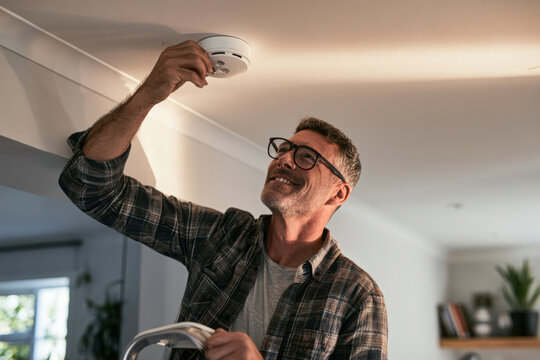 Homeowner testing a ceiling mounted smoke alarm to ensure reliable fire detection and household safety through routine maintenance.