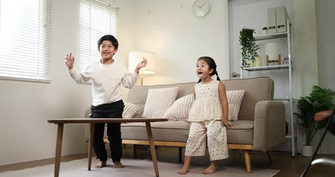 Asian mother sitting on the sofa, adjusting her son's red backpack before he leaves for school, illustrating a daily family routine and the nurturing aspect of parenting