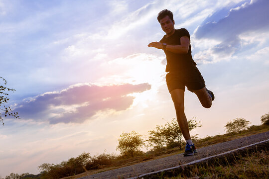 Silhouette of young man running sprinting on road. Fit runner fitness runner during outdoor workout with sunset background
