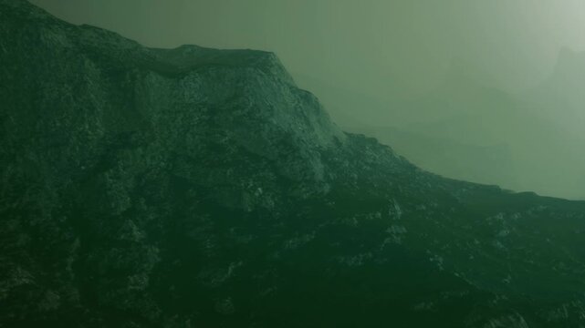 Fog covers the mountains early in the morning. The landscape appears mysterious and quiet as the light filters through the mist. A sense of stillness surrounds the scene.