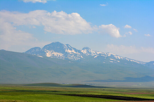 Beautiful mountain landscape with green grass and blue sky. Scenic landscape with green meadows, rolling hills, and snowy mountains in the background under a blue sky with white clouds