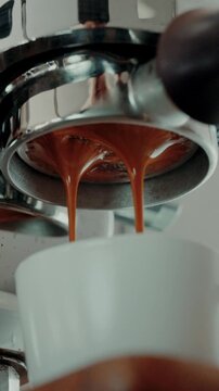 4K Pouring coffee stream from professional machine in cup. Barista man making double espresso, using filter holder. Flowing fresh ground coffee. Drinking roasted black coffee in the morning.Advertisin