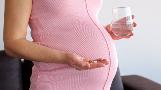 Pregnant woman holding a handful of prenatal vitamins and a glass of water, prioritizing maternal and fetal health during gestation and expecting motherhood