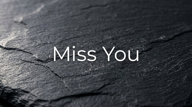 Miss You text on black slate stone background, emotional message on dark rock texture, minimalist mourning and remembrance concept