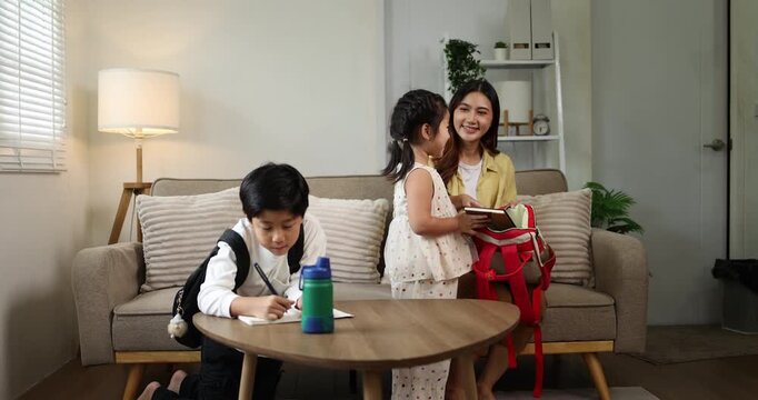 Asian mother and son preparing for school in a bright home setting, with the parent helping the child pack his red backpack and water bottle, showcasing family support and education responsibilities