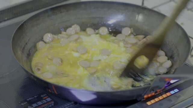 A scene of someone frying eggs, sausages, and garlic in an iron skillet on an induction cooktop to make fried rice.
