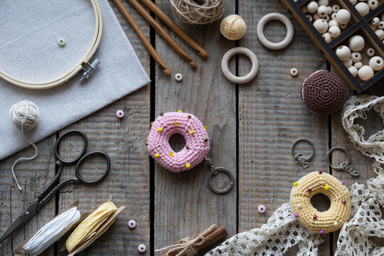 Flat lay knitting and crochet workspace with colorful donut shaped pincushions embroidery hoop scissors yarn lace and sewing accessories on rustic wooden background with copy space