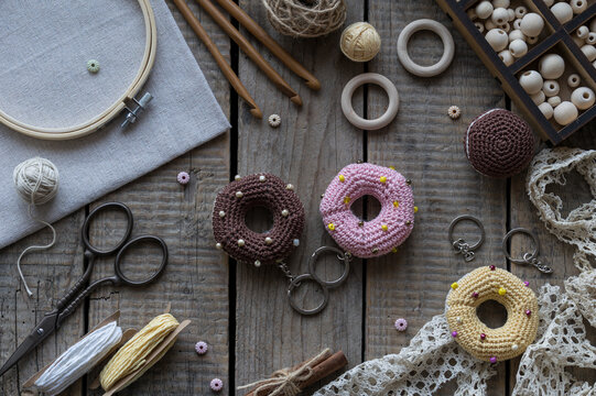 Handmade knitting and sewing accessories with colorful donut pincushions lace embroidery hoop scissors and yarn on rustic wooden background top view craft composition