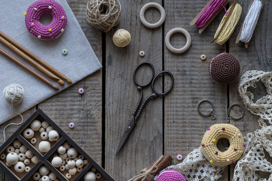 Handmade sewing and knitting workspace with colorful pincushions embroidery hoop lace scissors yarn and crochet accessories on wooden background flat lay style