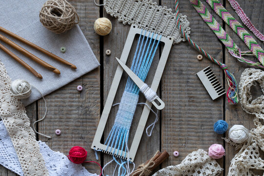 Flat lay weaving and macrame workspace with loom shuttle threads crochet hooks comb lace and craft accessories on rustic wooden table background