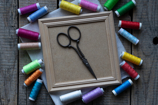 Vintage scissors on blank wooden frame surrounded by colorful sewing threads flat lay craft background with copy space for text or mockup design