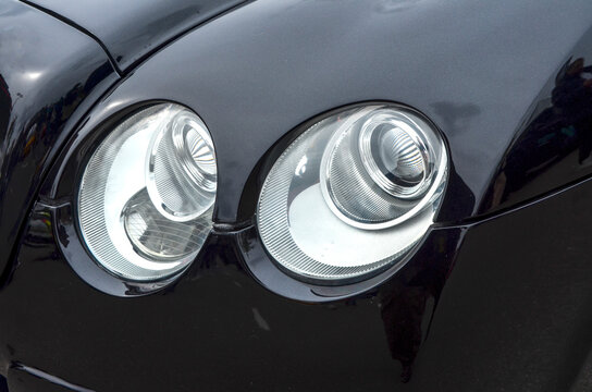 Close up of the dual round headlights on luxury black Bentley Continental GT, highlighting the detailed chrome projectors and the glossy finish of the vehicle front body