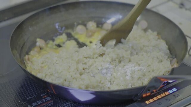 A scene of someone using an iron frying pan on an induction cooktop to stir fried rice.