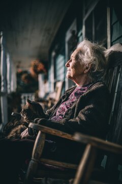 Elderly woman sits on porch with cat during afternoon light on a quiet day in her hometown, enjoying the warm ambiance of her surroundings